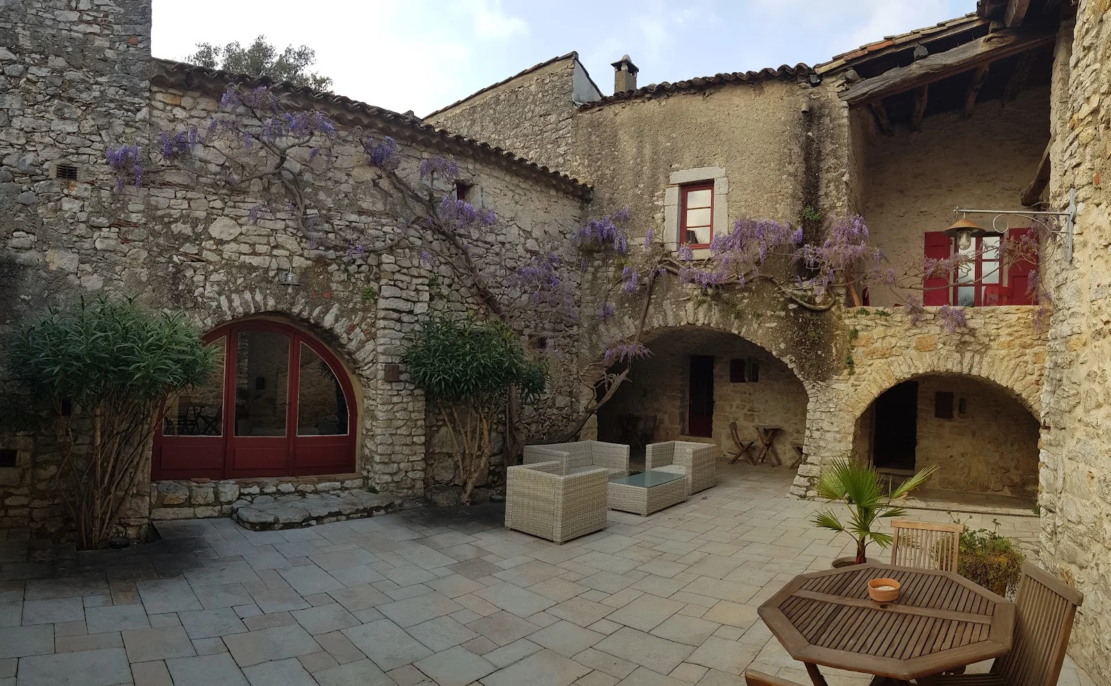 Cour intérieure du Domaine du Mas de Coulet ornée de glycines violettes et arcades en pierre, mariage Hérault