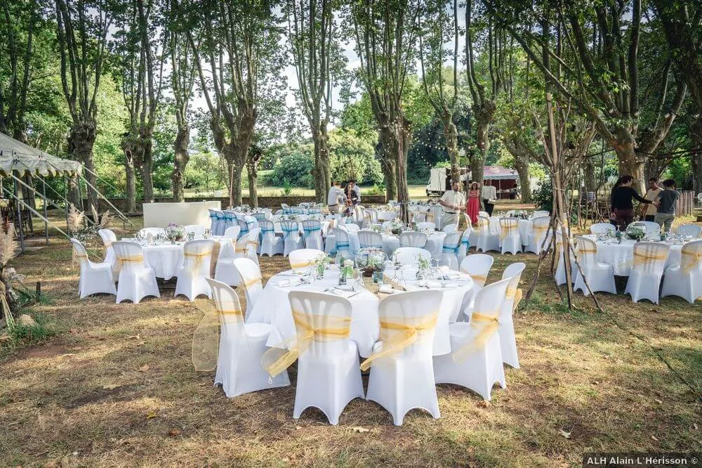 Tables rondes nappées blanc, chaises houssées, jardin arboré, ambiance festive Domaine Pech Laurier Quarante mariage Hérault Occitanie