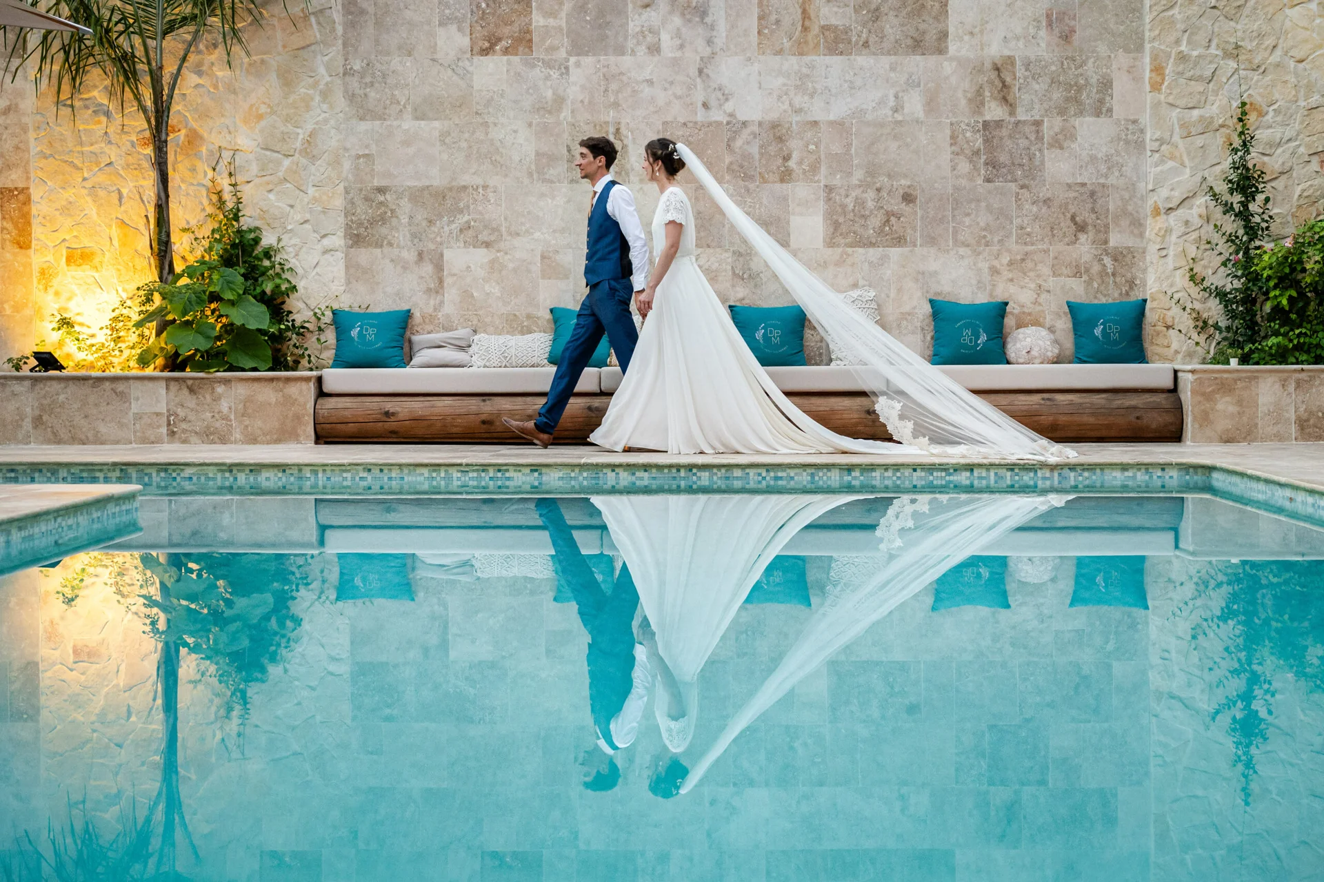 Couple de mariés longeant la piscine avec reflet dans l'eau au Domaine Le Petit Malherbes, mariage Hérault