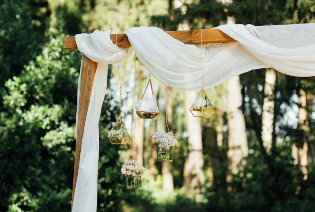 Arche de cérémonie en bois drapée de voile blanc avec suspensions dorées au Domaine Saint Hilaire en Hérault