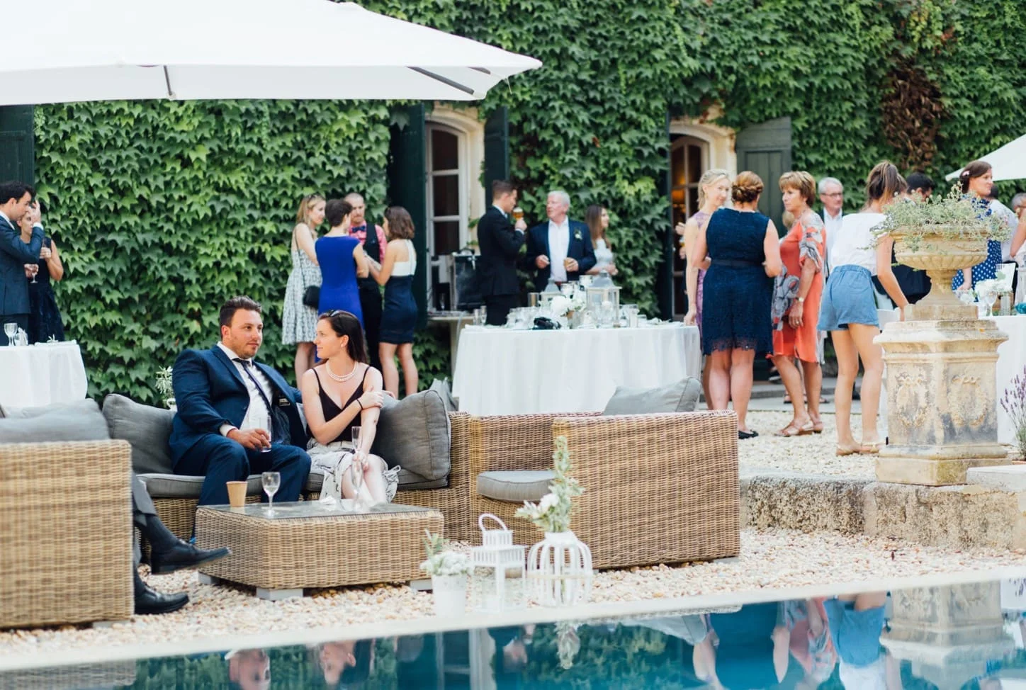 Cocktail de mariage en terrasse devant la façade en pierre couverte de lierre du Domaine Saint-Hilaire dans l'Hérault