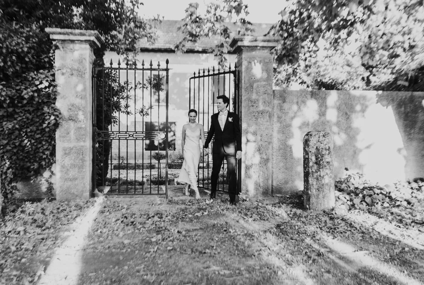 Mariés passant sous le portail en fer forgé du Domaine Saint-Hilaire dans l'Hérault, photo noir et blanc romantique