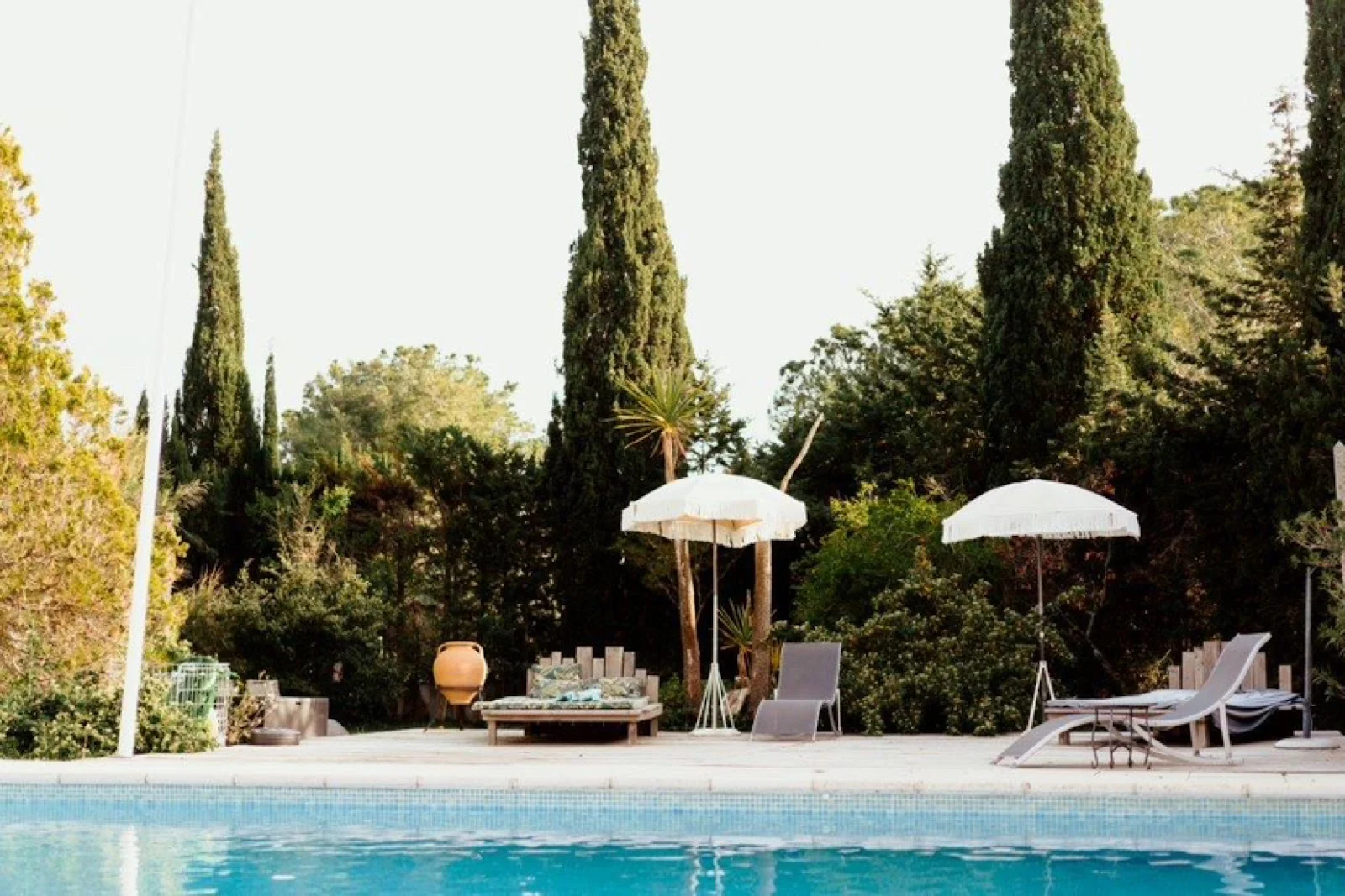 Piscine avec transats et parasols blancs entourée de cyprès au Domaine Saint Paul le Marseillais, lieu de mariage Hérault