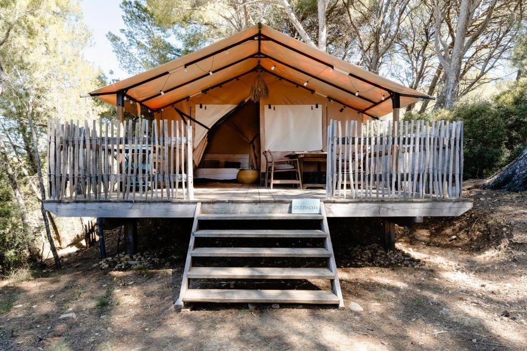 Tente safari glamping sur plateforme bois avec terrasse et guirlandes lumineuses dans les pins, hébergement mariage Domaine Saint Paul Hérault