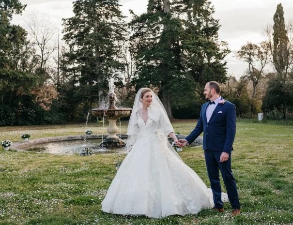 Couple de mariés devant la fontaine du parc de La Trésorière dans l'Hérault, robe volumineuse et costume bleu