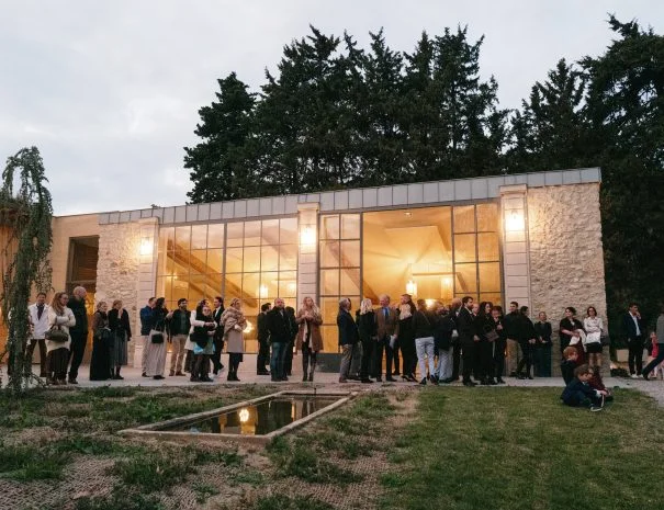 Pavillon en pierre et verre illuminé de La Trésorière avec miroir d'eau, invités rassemblés pour un mariage dans l'Hérault