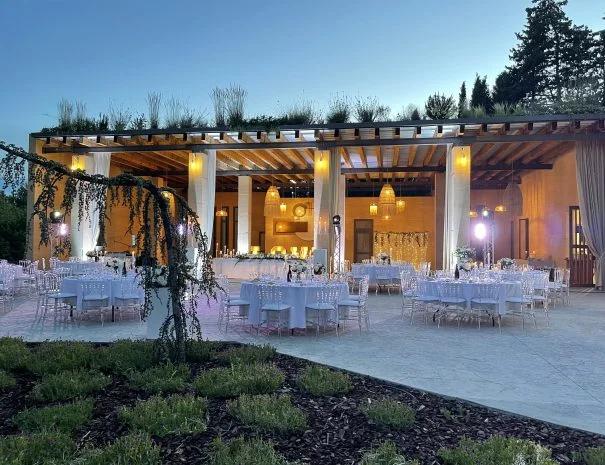 Salle de réception mariage La Trésorière sous pergola éclairée au crépuscule, tables dressées en blanc, Hérault