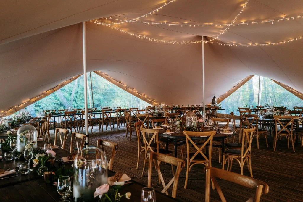 Tente de réception mariage La Trésorière Hérault avec guirlandes lumineuses et chaises en bois crossback