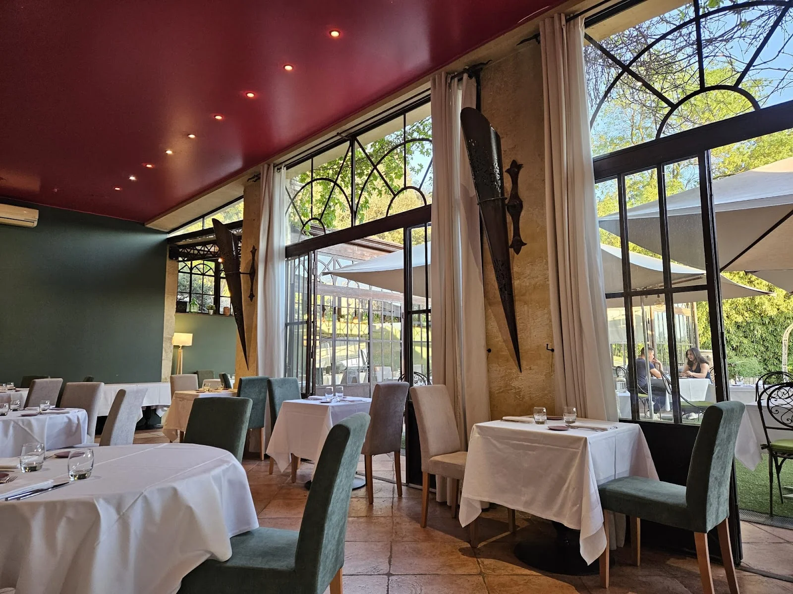 Salle intérieure du restaurant Le Grand Arbre Château de Bionne Hérault avec verrières et décoration élégante bordeaux et vert