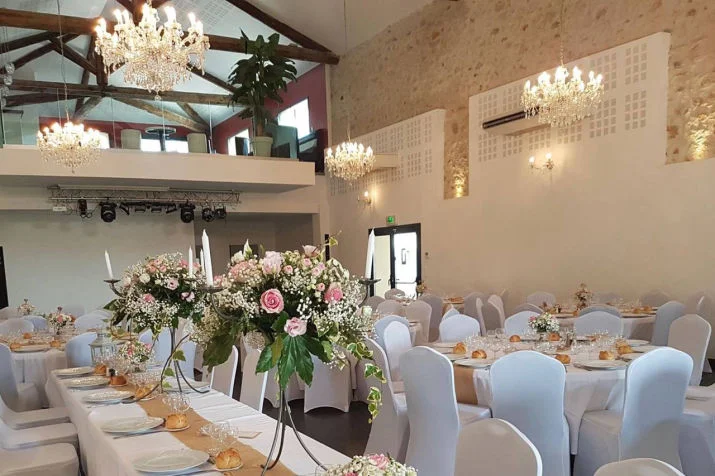 Salle de mariage du Mas de Laux avec lustres en cristal, poutres et décoration florale rose en Hérault