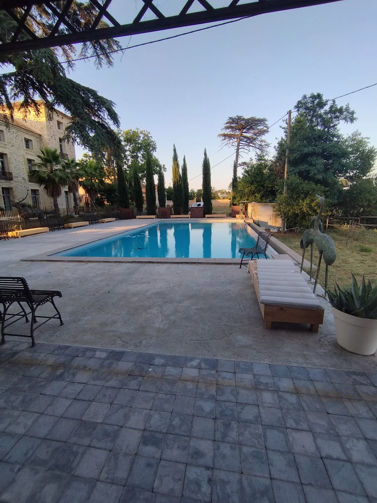 Piscine du domaine Les Castans au coucher du soleil pour un mariage en Hérault avec transats et sculptures