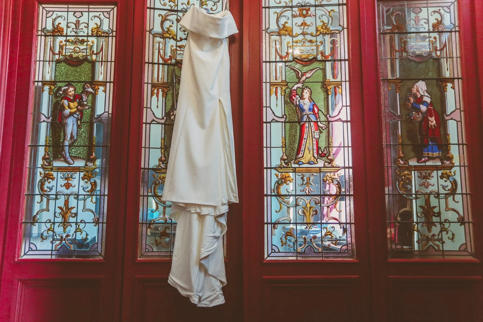 Robe de mariée suspendue devant le vitrail coloré du domaine Les Castans, lieu de mariage patrimonial en Hérault