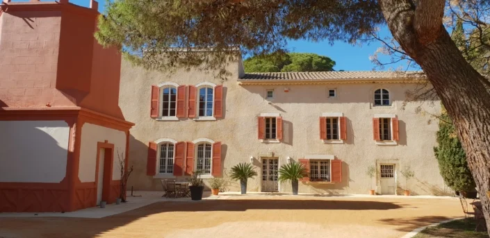 Façade principale du domaine Les Charmes de Bailly avec volets rouges et cour en gravier, lieu de mariage en Hérault Occitanie