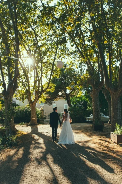 Mariés main dans la main sur l'allée arborée aux lanternes des Charmes de Bailly dans l'Hérault en lumière dorée