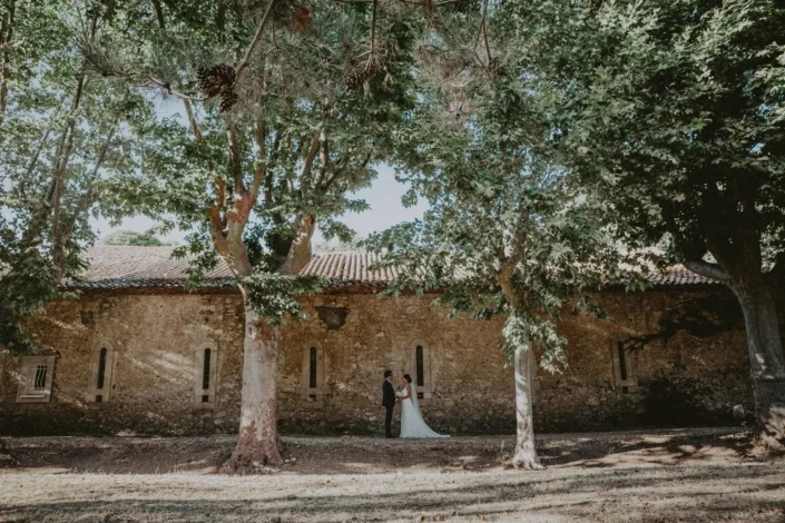 Couple de mariés devant le bâtiment en pierre ancienne du domaine Les Charmes de Bailly en Hérault, cérémonie mariage Occitanie