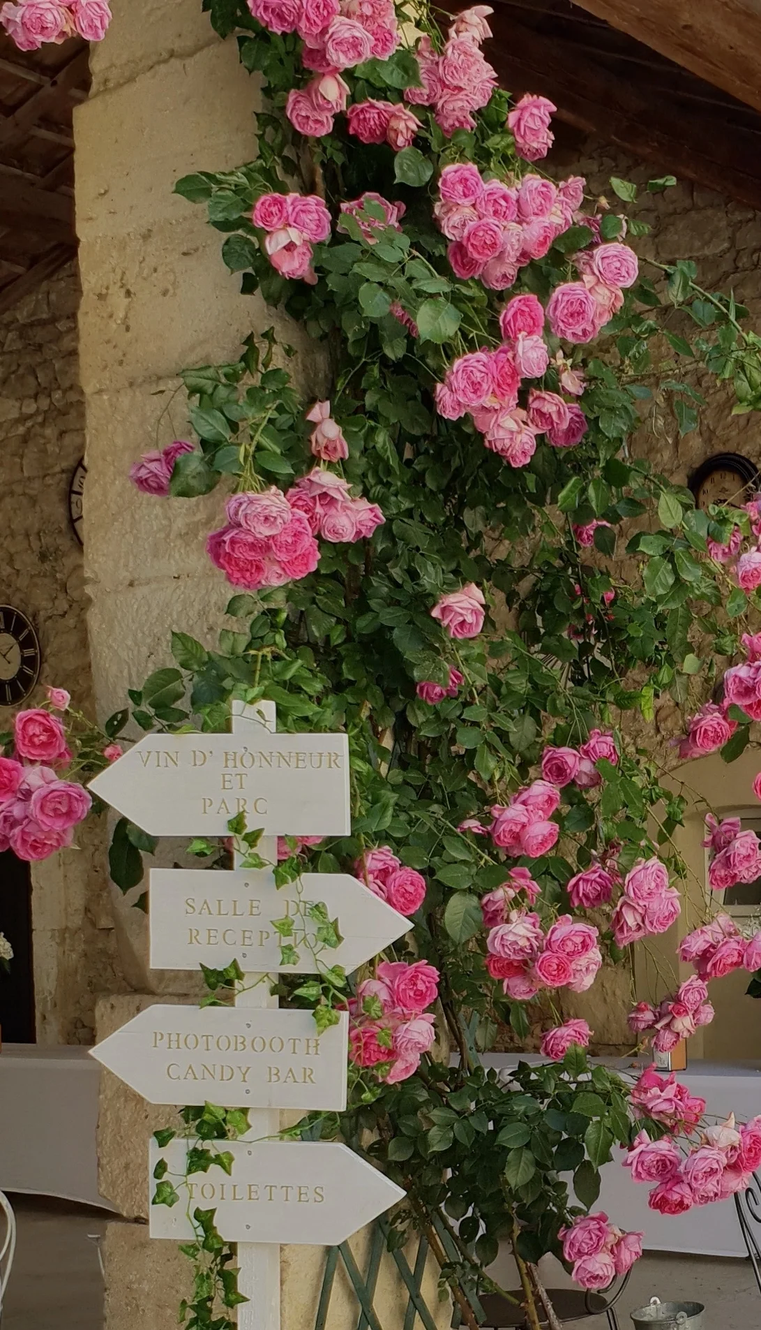 Panneau directionnel mariage entouré de rosiers grimpants roses sur pilier en pierre aux Charmes de Bailly, Hérault