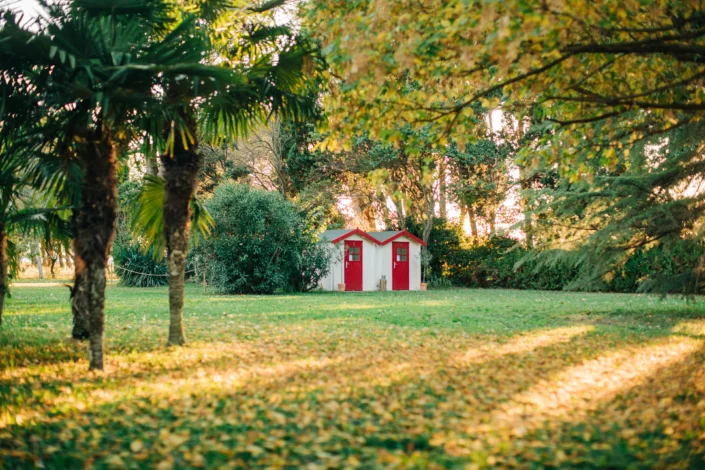 Parc verdoyant du domaine Les Charmes de Bailly en Hérault avec petit chalet blanc à portes rouges, jardin mariage Occitanie