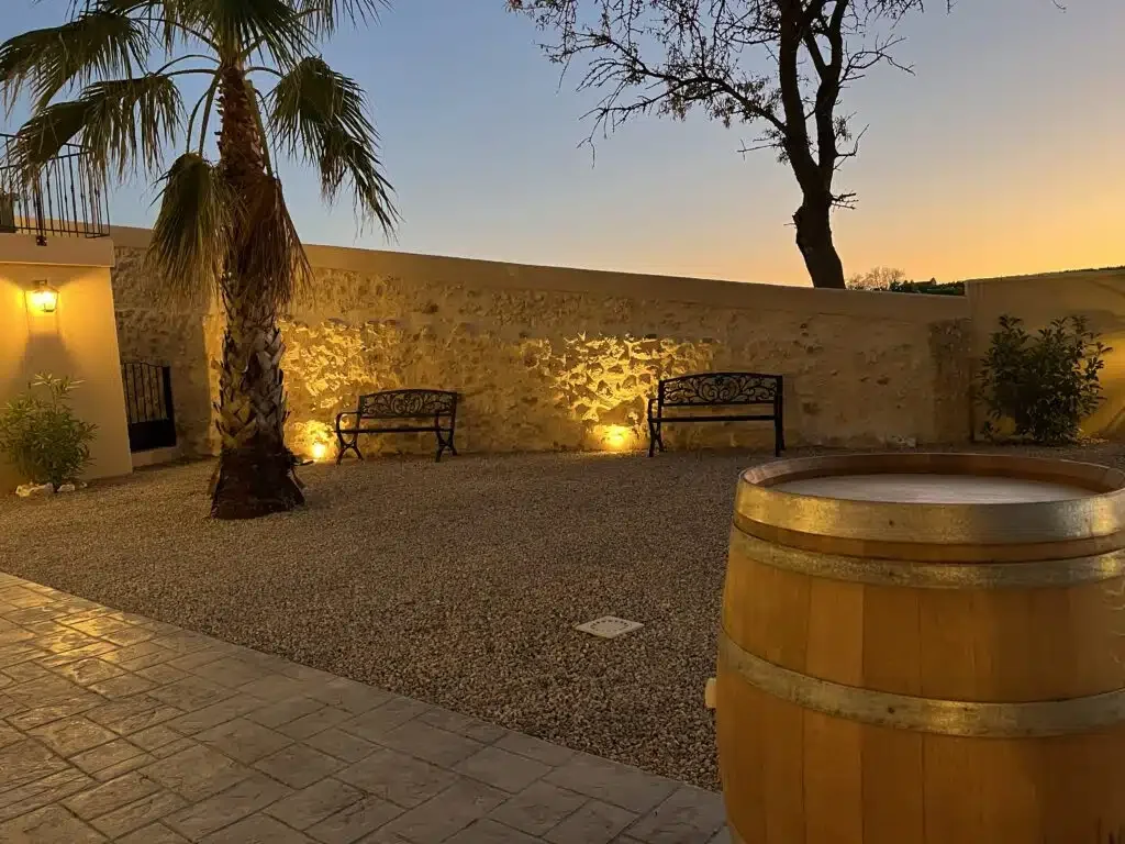 Cour extérieure des Granges Saint Paul au coucher du soleil avec tonneau, palmier et murs en pierre éclairés, Hérault