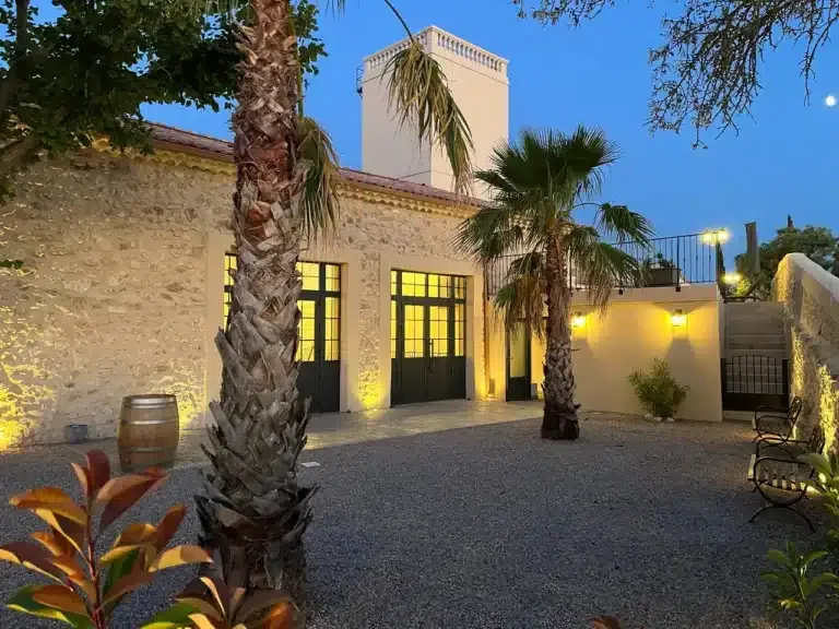 Cour intérieure nocturne des Granges Saint-Paul avec palmiers éclairés et façade en pierre, domaine mariage Hérault