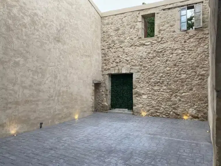 Cour intérieure pavée des Granges Saint Paul avec murs en pierre brute et porte végétalisée en lierre, Hérault