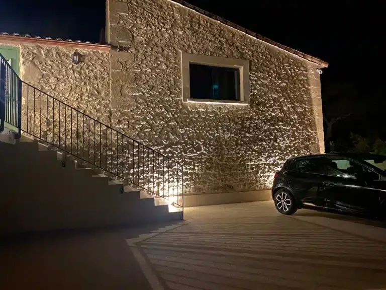 Façade en pierre du domaine Les Granges Saint Paul illuminée de nuit, escalier et parking