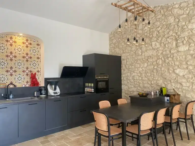 Salle à manger avec table 8 personnes, cuisine noire et mur en pierres - Les Granges Saint Paul Hérault