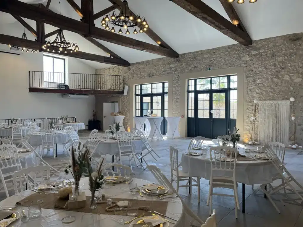 Salle de réception Les Granges Saint Paul dressée pour mariage avec tables rondes blanches et poutres apparentes, Hérault