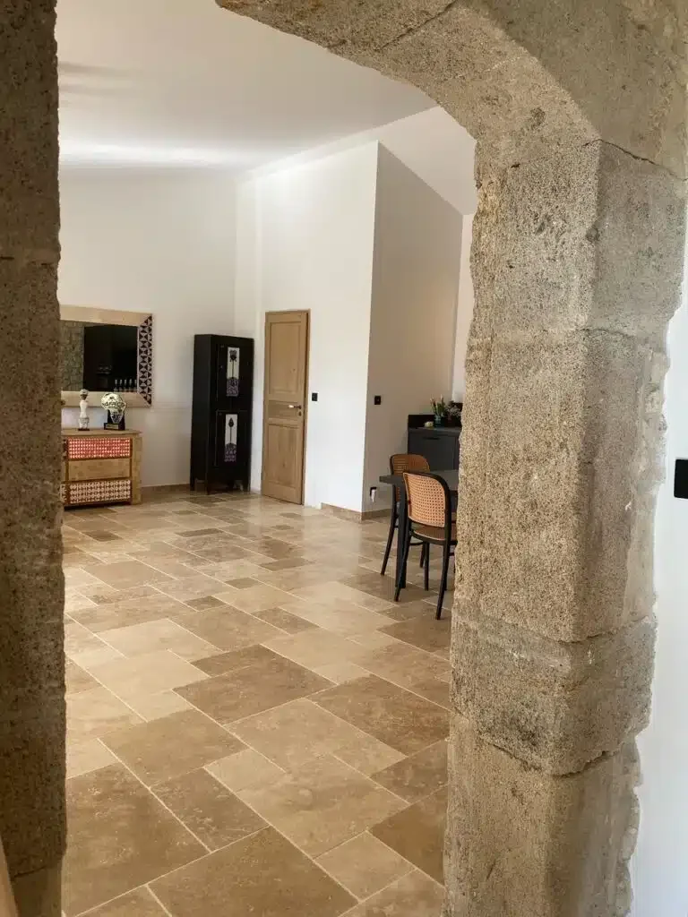 Séjour vu depuis l'arche en pierre avec sol en pierre beige - Les Granges Saint Paul Hérault