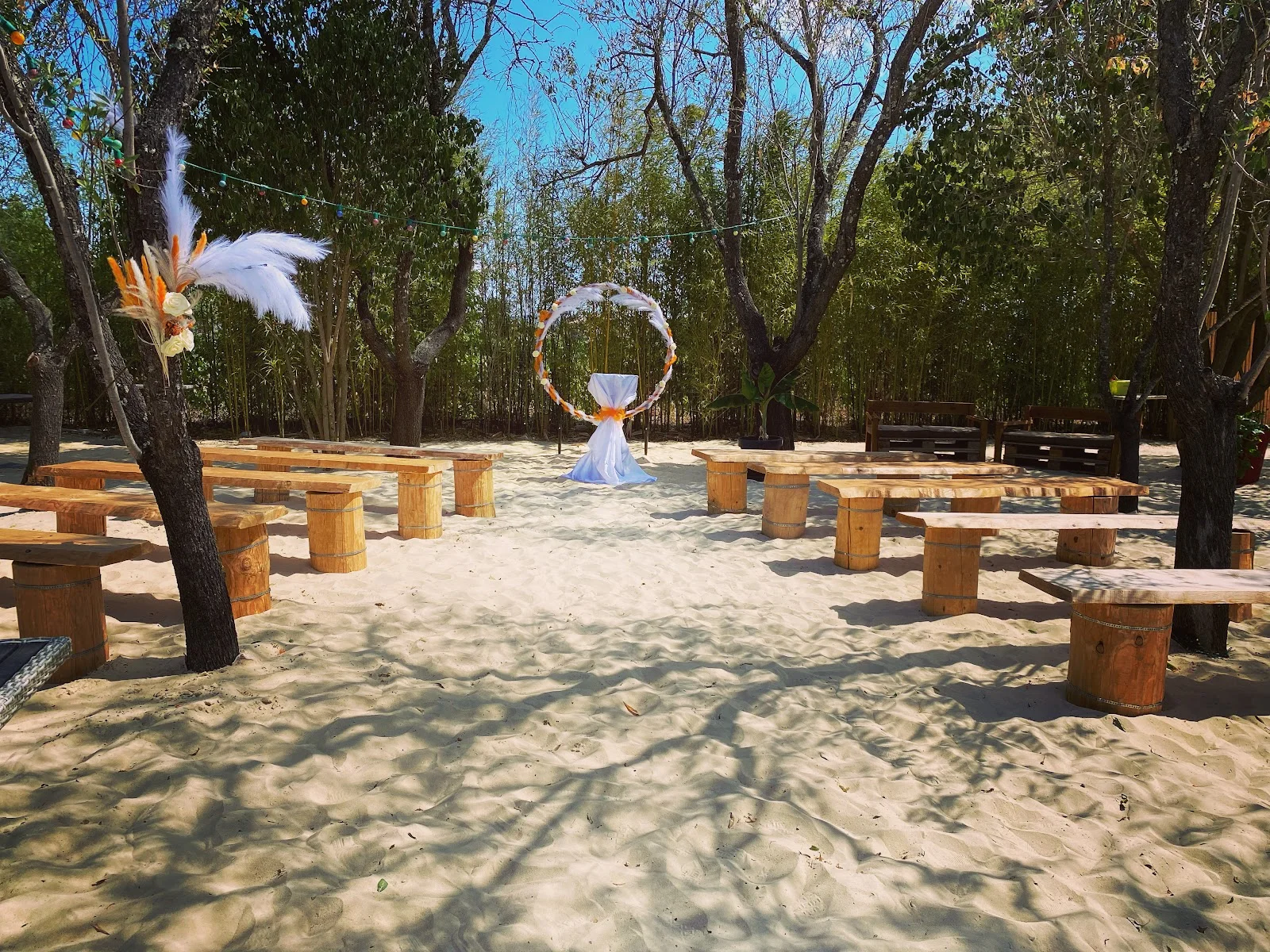 Espace cérémonie laïque sur sable blanc à L'Impensable Aniane, arche circulaire fleurie et bancs bois en Hérault