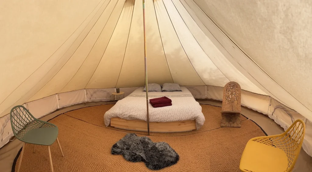 Intérieur bell tent glamping de L'Impensable Aniane, lit double sur estrade bois et décoration ethnique, mariage Hérault