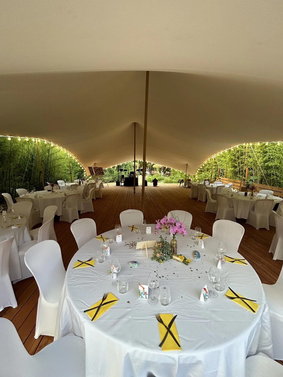Intérieur de la tente de mariage à L'Impensable Aniane, tables rondes dressées avec serviettes jaunes et orchidées, Hérault