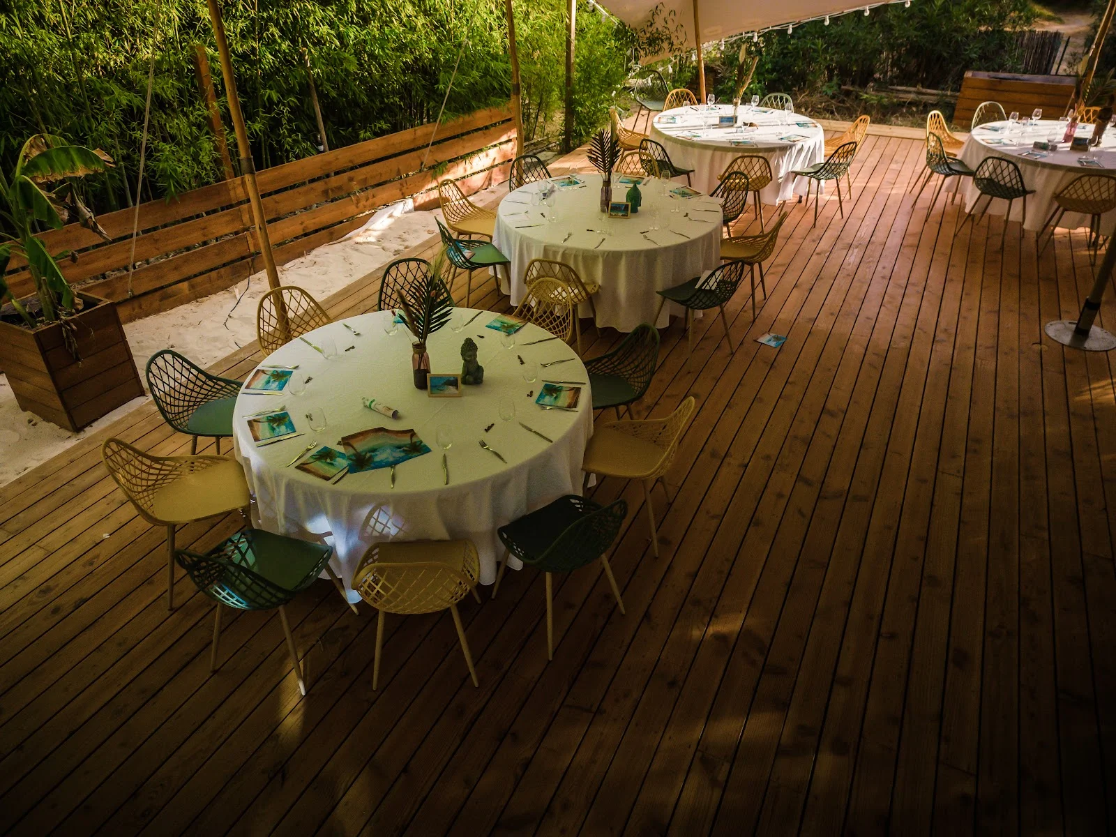 Vue plongeante sur les tables dressées de L'Impensable Aniane, chaises design et décoration tropicale sur terrasse bois, mariage Hérault