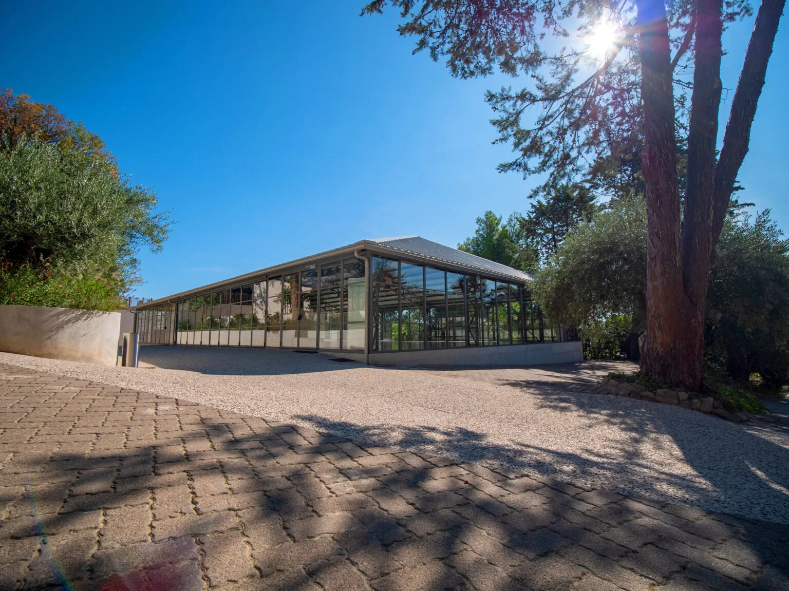 Façade vitrée de la salle de réception du Mas Aubrilha en plein soleil, domaine de mariage Hérault entouré de végétation méditerranéenne