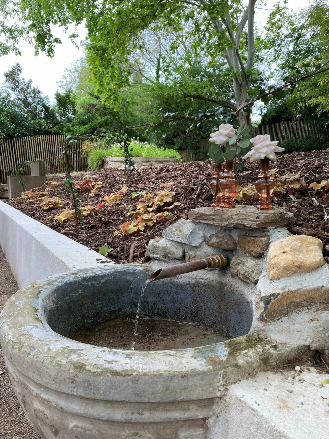 Fontaine en pierre ancienne décorée de roses, détail romantique du Mas Aubrilha pour mariage en Hérault