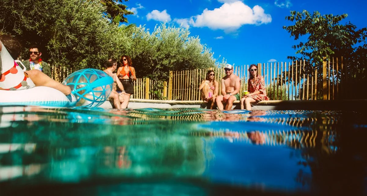 Groupe d'amis profitant de la piscine du Mas Aubrilha en Hérault lors d'une fête estivale sous ciel bleu