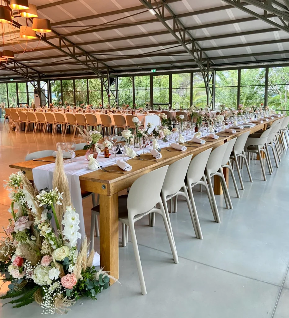 Salle de mariage du Mas Aubrilha décorée avec longues tables en bois, fleurs roses et blanches, herbes de pampa, Hérault
