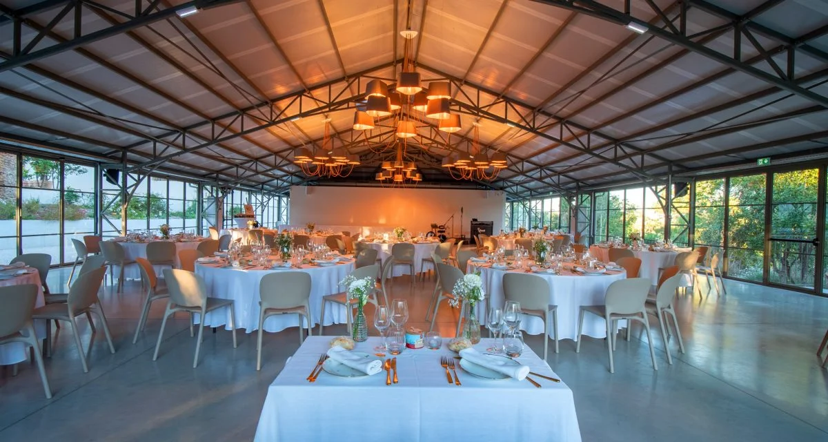 Salle de mariage du Mas Aubrilha en Hérault avec tables rondes en nappe blanche et lustres cuivrés dorés