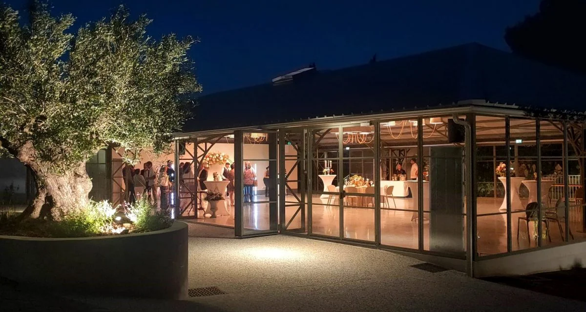 Salle de réception du Mas Aubrilha en Hérault illuminée de nuit avec oliviers éclairés et convives à l'intérieur