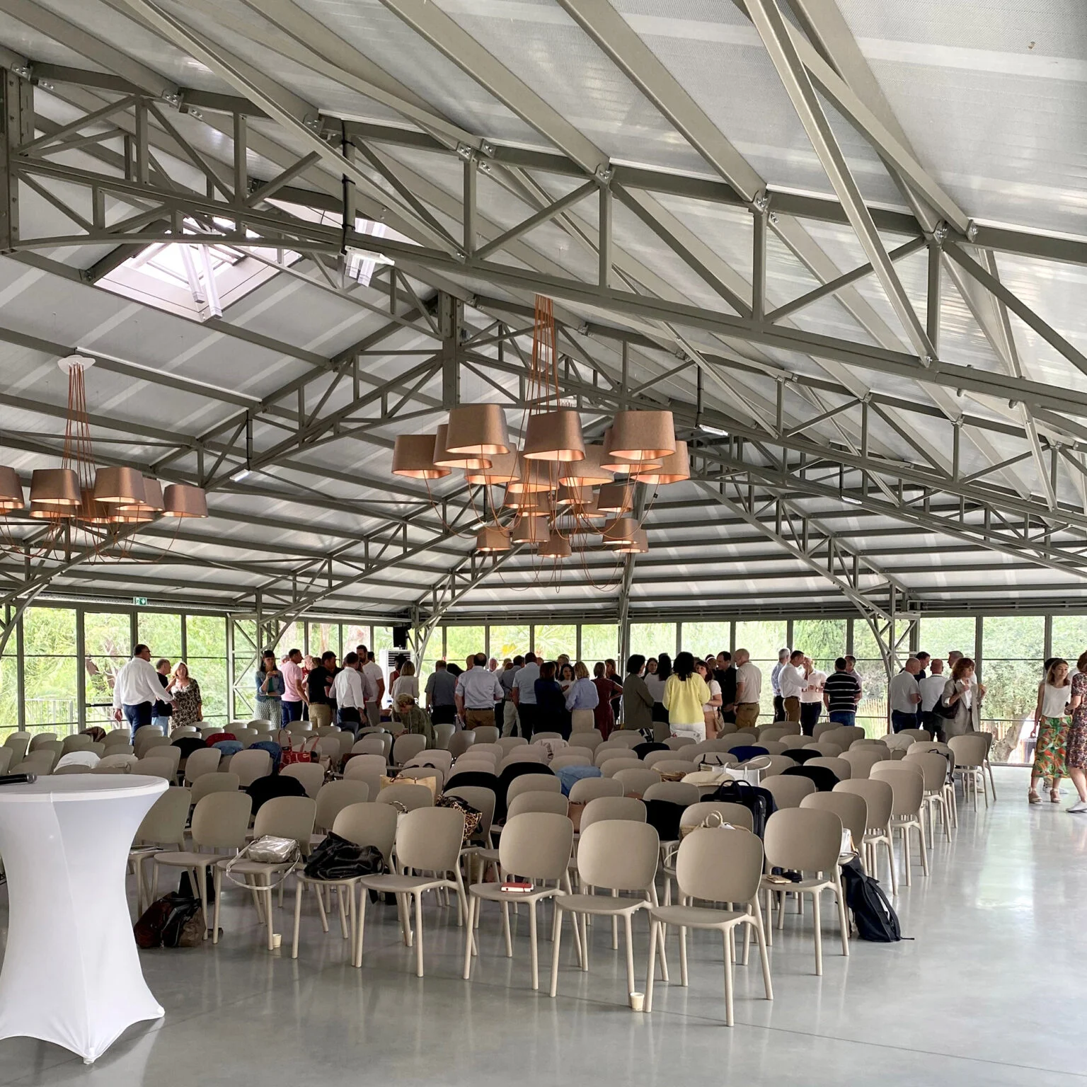 Salle de réception Mas Aubrilha en configuration conférence avec invités, luminaires design et baies vitrées sur jardins, Hérault