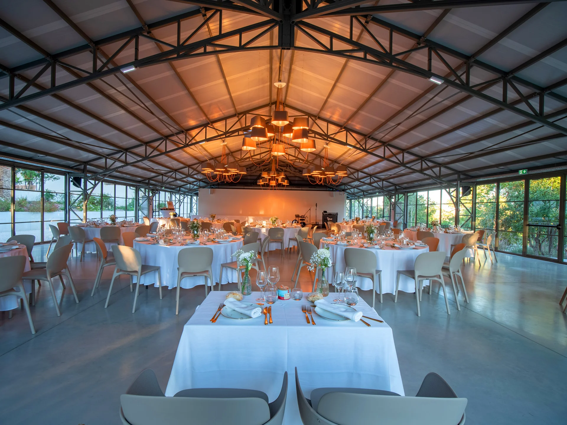 Salle de réception du Mas Aubrilha en Hérault dressée avec tables rondes en nappe blanche et lumière chaude dorée