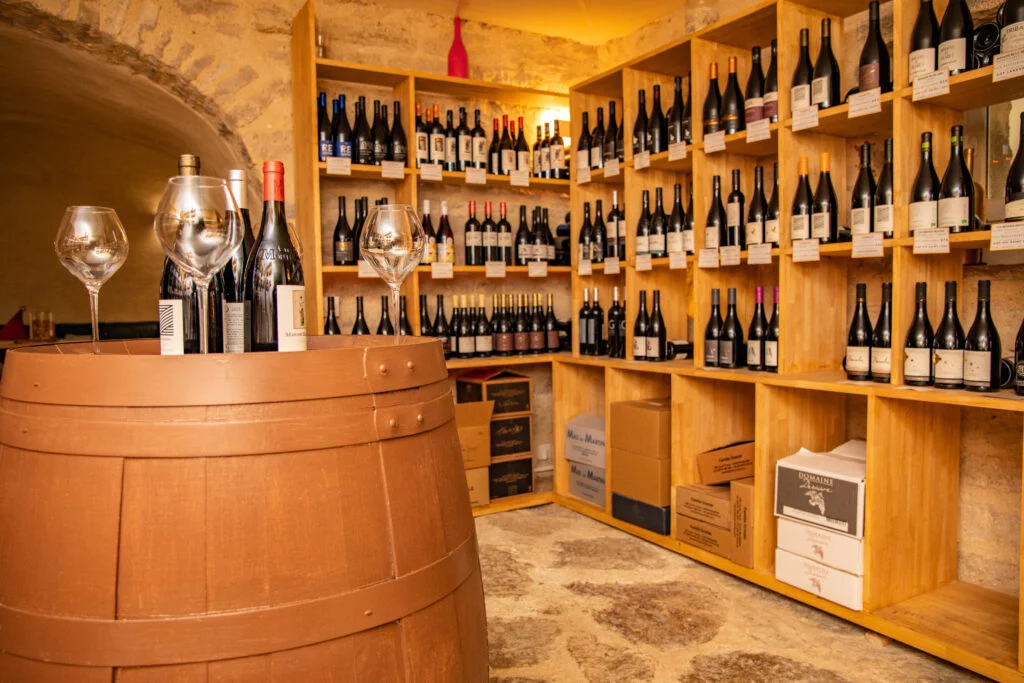 Cave à vins du Mas de Baumes avec tonneau, verres et étagères de bouteilles sous voûte en pierre, dégustation mariage Hérault