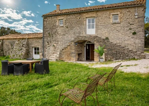 Vue extérieure du Mas de Baumes en pierre avec jardin verdoyant et mobilier de jardin, lieu de mariage Hérault