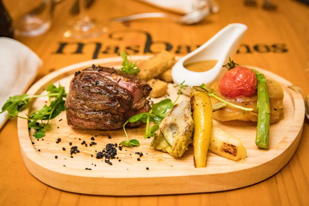Plat gastronomique du Mas de Baumes : viande grillée, légumes rôtis et truffe noire sur plateau bois, restaurant mariage Hérault