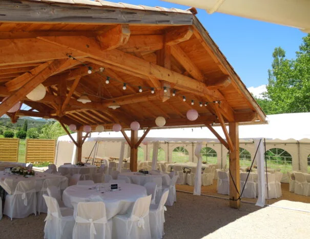 Espace réception en charpente bois avec guirlandes et lampions roses pour mariage au Mas de Pradines, Hérault