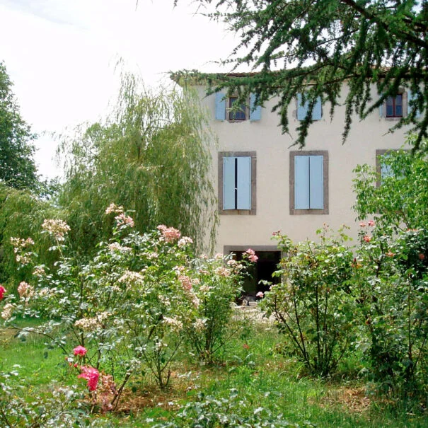 Façade aux volets bleus du Mas de Pradines entourée de rosiers en fleurs, jardin mariage Hérault