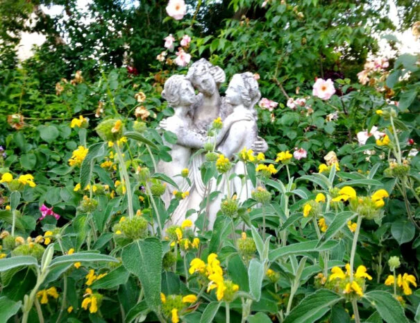 Statue des Trois Grâces entourée de fleurs jaunes dans le jardin du Mas de Pradines - Hérault