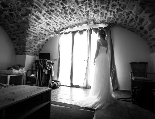 Mariée de dos en robe blanche dans une chambre voûtée en pierre au Mas de Pradines, Hérault – préparatifs mariage