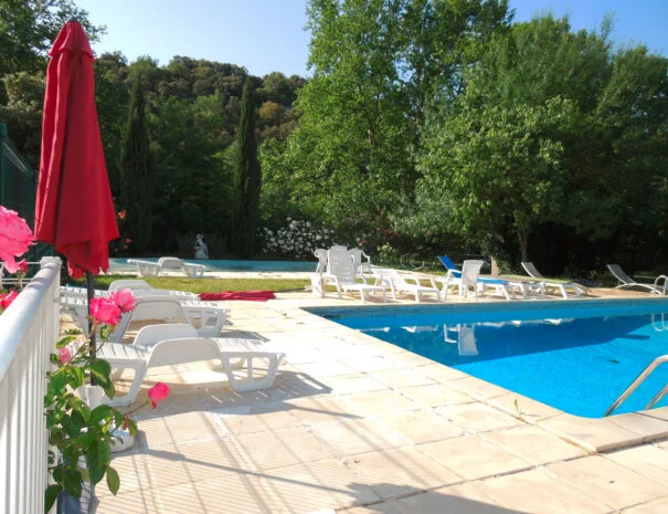 Piscine du Mas de Pradines entourée de transats, rosiers et cyprès avec vue sur les collines de l'Hérault