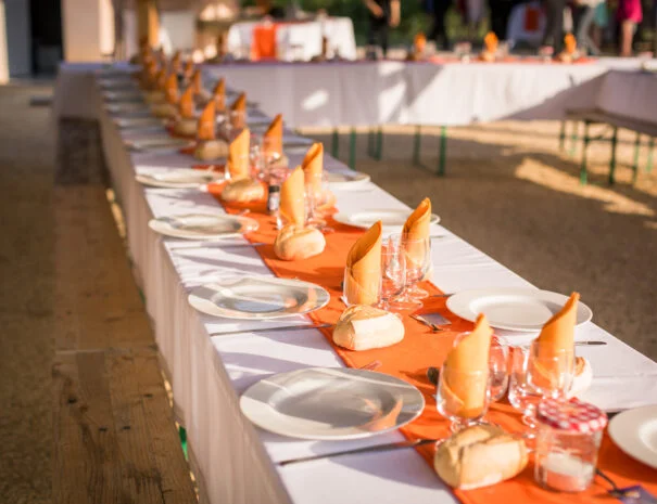 Table banquet extérieure dressée avec nappes blanches et chemin de table orange pour mariage au Mas de Pradines, Hérault