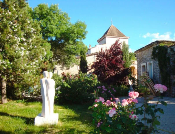 Vue globale du Mas de Pradines en Hérault avec bâtisse en pierre, tour et sculpture de couple dans le jardin